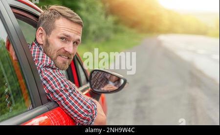 Un homme regarde de l'intérieur d'une voiture rouge sur une autoroute. Banque D'Images