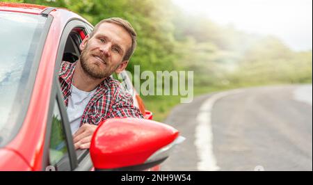 Un homme regarde de l'intérieur d'une voiture rouge sur une autoroute. Banque D'Images