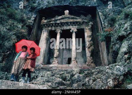 Turquie. Fethiye. Ruines de la tombe d'Amyntas. Deux jeunes filles debout avec un parapluie. Banque D'Images