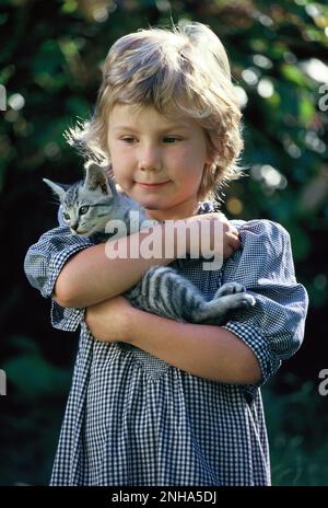 Enfants. Petite fille à l'extérieur dans le jardin tenant son chat d'animal de compagnie. Banque D'Images