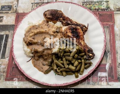 Des pilons de poulet épicés cuits au four, une purée de pommes de terre, de la sauce au poulet et des haricots verts sur un napperon parisien à une table à Taylors Falls, Minnesota, États-Unis. Banque D'Images