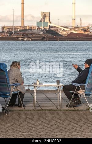 Un homme et une femme sont assis sur deux chaises près du front de mer avec vue sur l'acier TATA à IJmuiden pays-Bas Banque D'Images