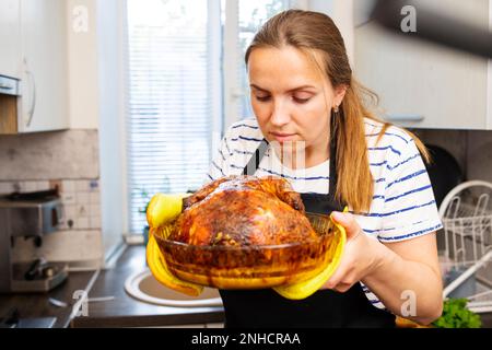 Femme en tablier noir tenant un plat avec un poulet rôti au four Banque D'Images