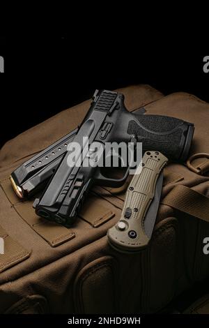 Un pistolet, des cartouches pour lui et un couteau pliant sur un sac à dos marron. Kit d'auto-défense et de survie. Armes à feu et armes à feu à bordure compacte. Fond noir Banque D'Images