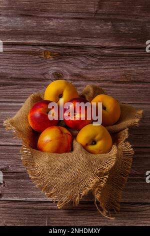 Groupe de nectarines fraîches sur un tissu de raphia avec un fond en bois sombre Banque D'Images