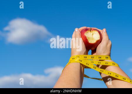 Femme tenant une pomme mordue dans ses mains avec un mètre ruban et un ciel avec des nuages en arrière-plan, concept d'un esclave de régime Banque D'Images