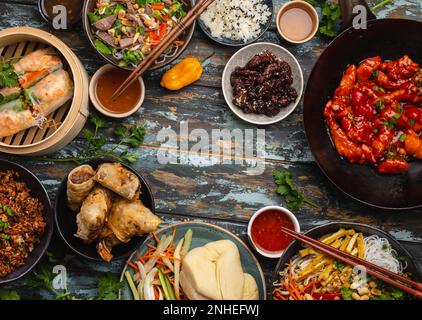 Ensemble de plats chinois variés sur la table : poulet aigre et sucré dans une poêle à wok, dim sum, rouleaux de printemps, nouilles, salade, riz, petits pains cuits à la vapeur. Style asiatique Banque D'Images