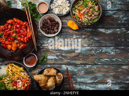 Ensemble de plats chinois variés sur la table : poulet aigre et sucré dans une poêle à wok, dim sum, rouleaux de printemps, nouilles, salade, riz, petits pains cuits à la vapeur. Style asiatique Banque D'Images