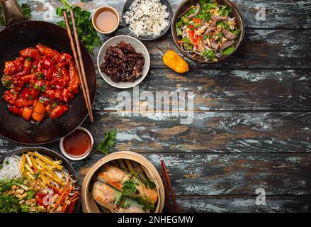 Ensemble de plats chinois variés sur la table : poulet aigre et sucré dans une poêle à wok, dim sum, rouleaux de printemps, nouilles, salade, riz, petits pains cuits à la vapeur. Style asiatique Banque D'Images