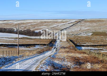 La neige couvrait la route rurale qui s'enroule à travers un paysage de montagne gelé au soleil d'hiver Banque D'Images