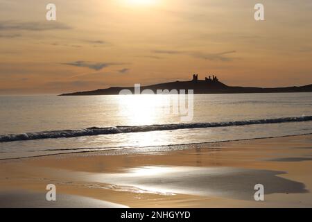 Château de Dunstanburgh au lever du soleil à travers la baie d'Embleton, Northumberland Banque D'Images