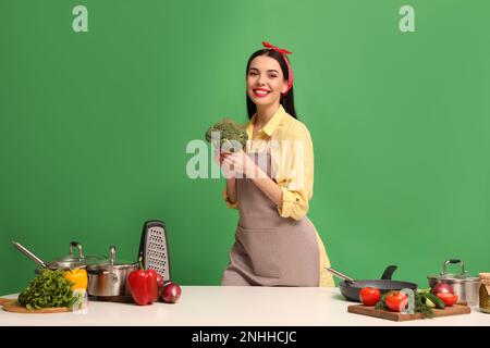 Jeune femme au foyer avec des légumes et différents ustensiles sur fond vert Banque D'Images