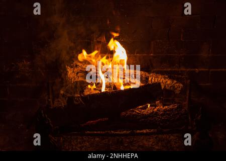 Un feu intérieur torrenant avec des flammes orange dans une cheminée à bois avec grille de cheminée à foyer métallique Banque D'Images