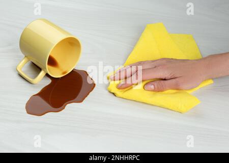 Femme nettoyant le café renversé sur une table en bois blanc, gros plan Banque D'Images