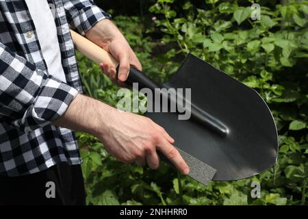 Homme affûtant la pelle à l'extérieur, gros plan. Outils de jardinage Banque D'Images