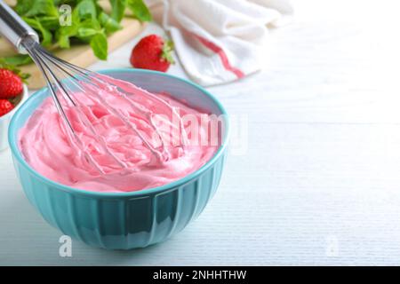 Fouetter de la crème à la fraise avec un fouet en ballon sur une table en bois blanc, en gros plan. Espace pour le texte Banque D'Images