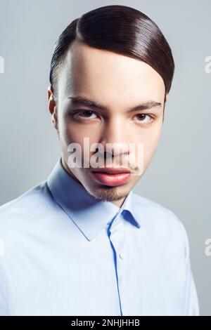 Portrait d'un jeune beau et beau homme sérieux avec moustache avec une coiffure rétro classique, regardant l'appareil photo, portant une chemise bleue. Prise de vue en studio isolée sur fond gris. Banque D'Images