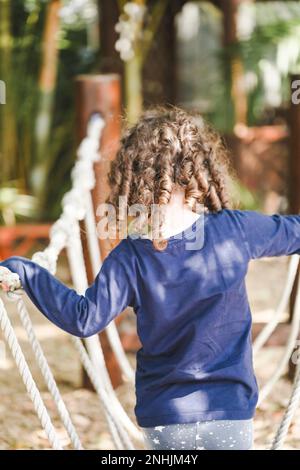 Enfant d'âge préscolaire jouant sur la corde balançoire. Magnifique jardin tropical de jardin d'enfants. Banque D'Images