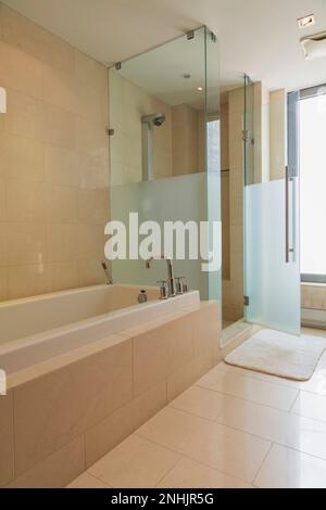 Salle de bains avec sol carrelé en marbre, baignoire blanche dans un boîtier en marbre et cabine de douche en verre à l'intérieur d'un luxueux appartement de grand standing moderne de plusieurs étages. Banque D'Images