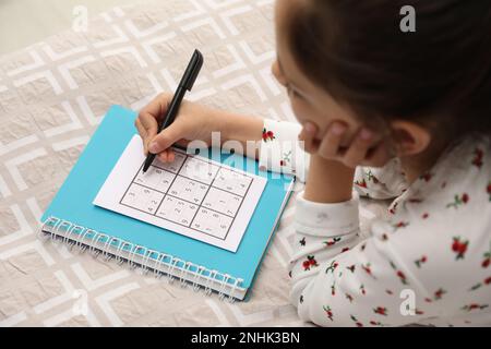 Petite fille résoudre sudoku puzzle sur le lit Banque D'Images