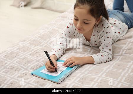 Petite fille résoudre sudoku puzzle sur le lit à la maison Banque D'Images