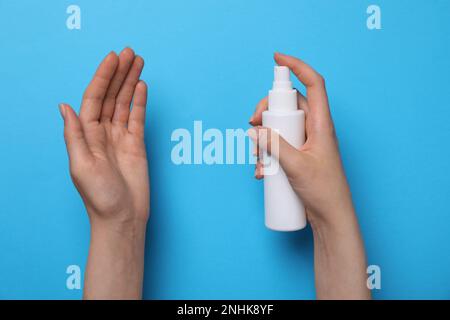 Femme pulvérisant un antiseptique à la main sur fond bleu clair, gros plan. Équipement de sécurité Banque D'Images