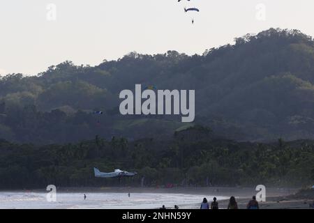 Un petit avion se touche avec élégance sur la plage de sable tandis que des parachutes colorées transportant des parachutistes flottent lentement vers le sol, un incroyable spectateur Banque D'Images