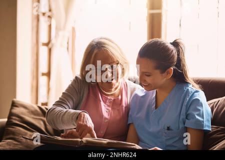 Donner vie à l'histoire. une infirmière et une femme âgée regardant ensemble un album photo. Banque D'Images