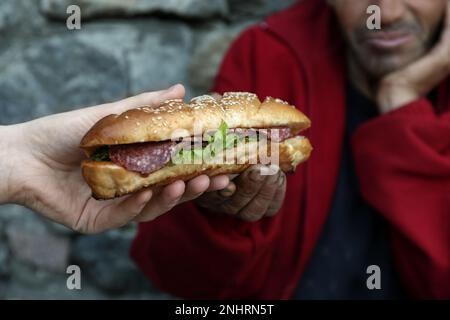 Femme donnant le pauvre homme sans-abri sandwich dans la rue, à proximité Banque D'Images