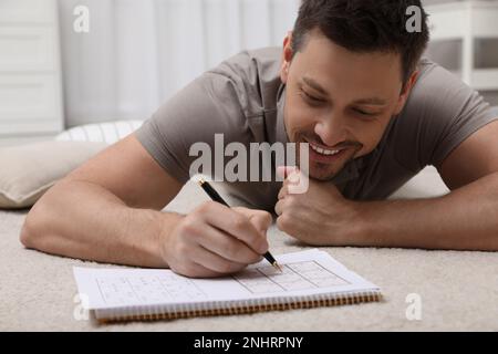 Homme résolvant le sudoku sur le sol à la maison Banque D'Images