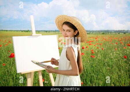 Petite fille peinture sur chevalet dans beau champ de pavot Banque D'Images