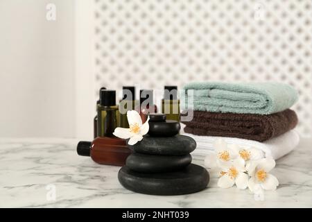 Pierres spa noires, belles fleurs de jasmin, serviettes et produits de soin de la peau sur une table en marbre blanc Banque D'Images