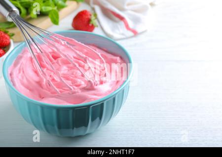 Fouetter de la crème à la fraise avec un fouet en ballon sur une table en bois blanc, en gros plan. Espace pour le texte Banque D'Images