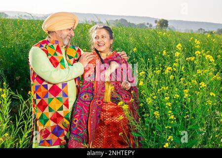 Heureux senior Pendjabi sikh couple portant des tissus colorés debout ensemble sur le terrain agricole. Se regardant l'un l'autre. Banque D'Images