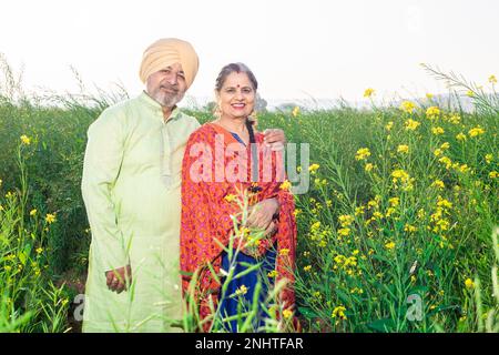 Portrait d'un couple de sikh Panjabi senior heureux debout ensemble dans le domaine agricole. Regarder l'appareil photo. Banque D'Images