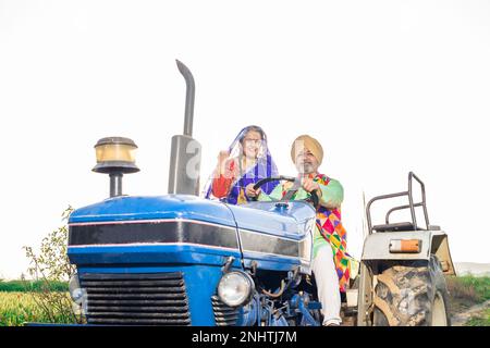 Joyeux couple de panjabi sikh senior conduisant un tracteur sur le terrain agricole en extérieur. Copier l'espace. Banque D'Images