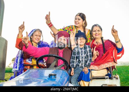 Bonne famille paysanne de punjabi sikh assise sur un tracteur dansant et célébrant à l'extérieur. Concept de prospérité. Banque D'Images