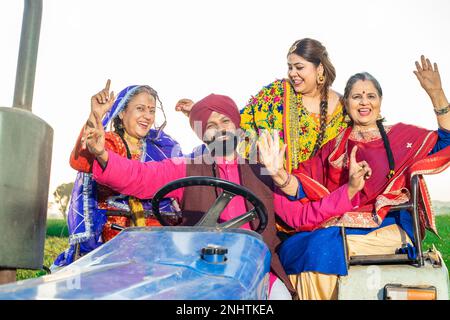 Bonne famille paysanne de punjabi sikh assise sur un tracteur dansant et célébrant à l'extérieur. Concept de prospérité. Banque D'Images