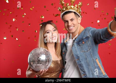 Couple heureux avec boule disco et confetti sur fond rouge Banque D'Images