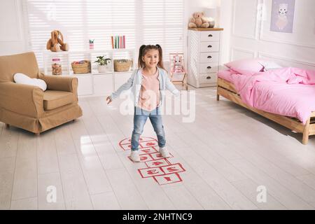 Adorable petite fille jouant au hopscotch à la maison Banque D'Images