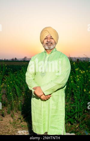 Portrait d'un homme pendjabi sikh heureux senior debout bras croisés portant le turban et le kurta regardant la caméra sur le champ de l'agriculture. Banque D'Images