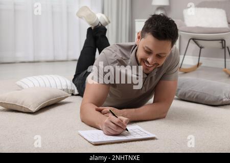 Homme résolvant le sudoku sur le sol à la maison Banque D'Images