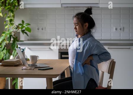 Une jeune femme asiatique fatiguée se sente fatiguée du travail sur ordinateur portable dans une mauvaise posture massante mal de dos. Banque D'Images