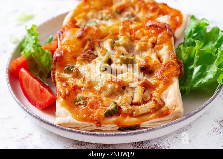 Mini pizza pour enfants, petites tartes ouvertes avec jambon, sauce tomate, mozzarella et fromage dans un panier sur fond clair. Banque D'Images