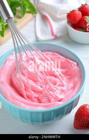 Fouetter de la crème à la fraise avec un fouet en ballon sur une table en bois blanc, en gros plan Banque D'Images