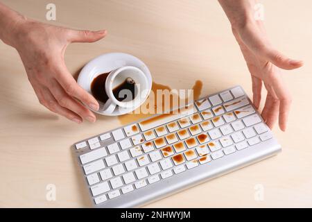 Femme avec du café renversé sur le clavier d'ordinateur à la table en bois, au-dessus de la vue Banque D'Images