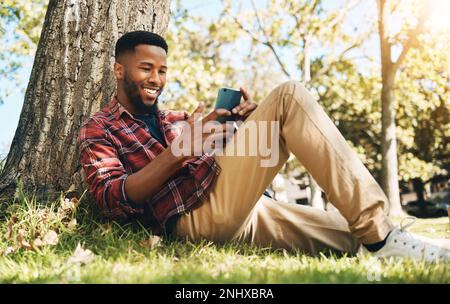 Homme noir, téléphone et détente dans un parc pour les médias sociaux, la communication ou le chat allongé sur l'herbe verte. Heureux Africain américain homme avec Banque D'Images