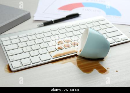 Tasse de café renversée sur le clavier de l'ordinateur sur une table en bois blanc Banque D'Images
