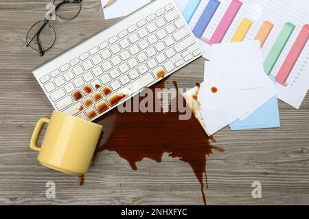 Tasse de café renversé sur le clavier de l'ordinateur sur le bureau en bois, plat Banque D'Images