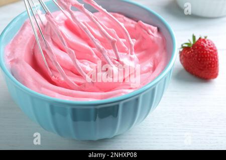 Fouetter de la crème à la fraise avec un fouet en ballon sur une table en bois blanc, en gros plan Banque D'Images
